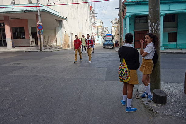 Havana, Cuba.  February 14, 2016.  Two young women talk as a group of young men cross the street and approach them.