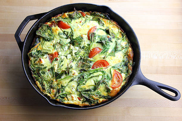 omelet A freshly made spring vegetable frittata in a cast iron pan set on a wooden surface frittata stock pictures, royalty-free photos & images