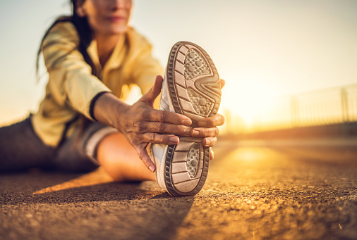 Close-up of athlete's sports shoe during stretching exercises on a road at sunset.
