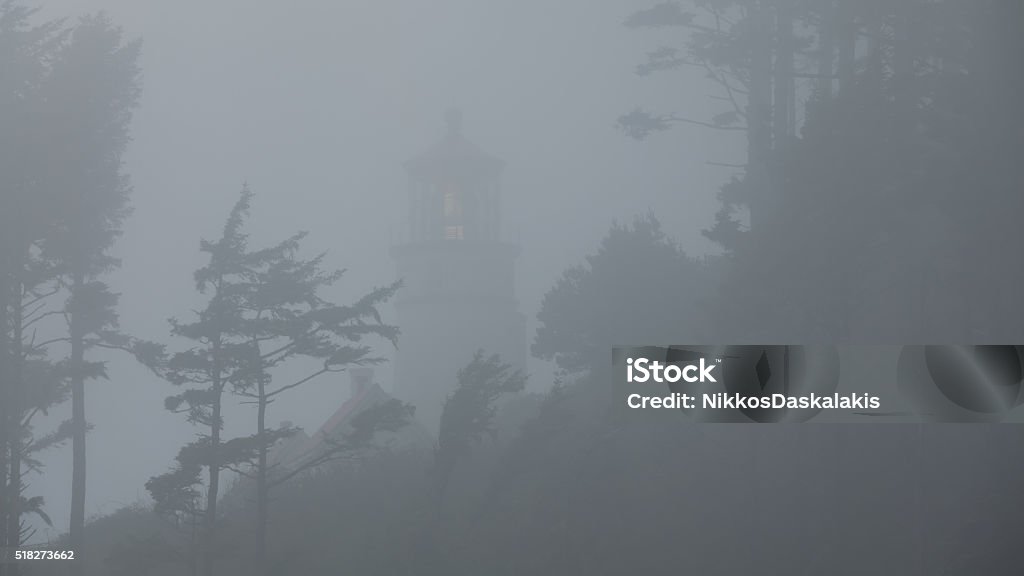 Heceta Head lighthouse in the fog The low fog paints a gloomy but beautiful landscape with the faint light from the lens of the lighthouse Oregon - US State Stock Photo