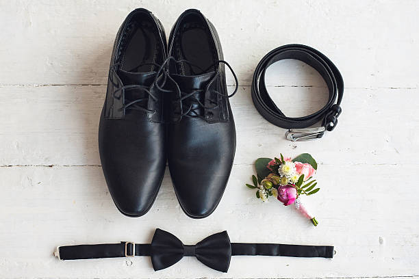 Close up of modern man accessories Close up of modern man accessories. Black bowtie, leather shoes, belt and flower boutonniere on white wood rustic background. Set for formal style of wearing isolated on white background. buttonhole flower stock pictures, royalty-free photos & images