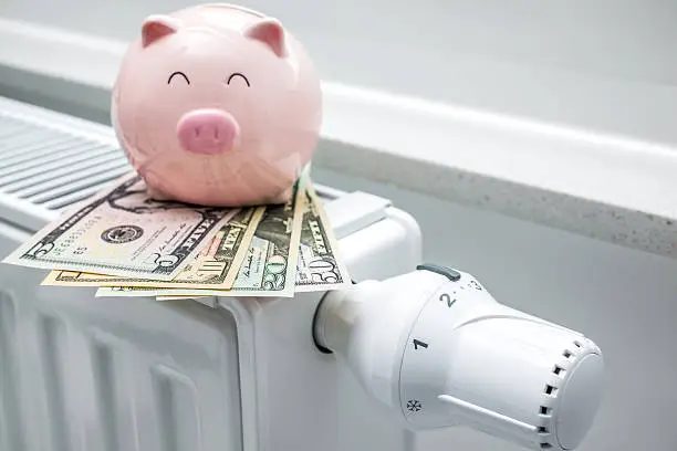 Heating thermostat with piggy bank and money, Expensive heating costs concept