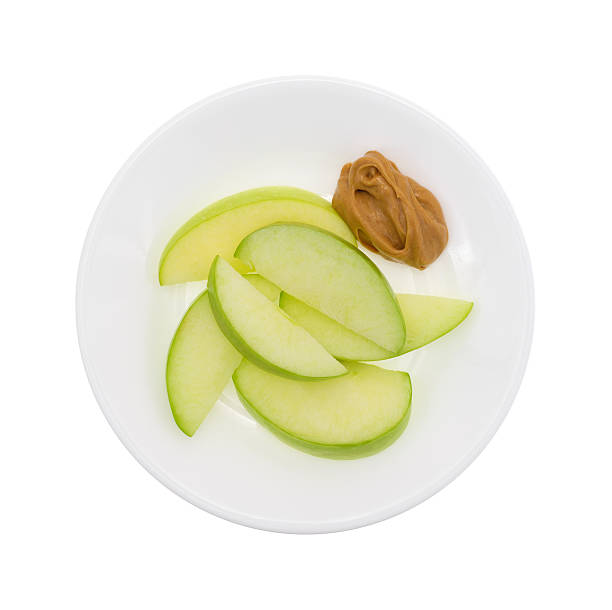 Green apple slices on dish with peanut butter top view Top view of a group of green apple slices on a dish with a small amount of peanut butter for dipping isolated on a white background. green apple slice overhead stock pictures, royalty-free photos & images
