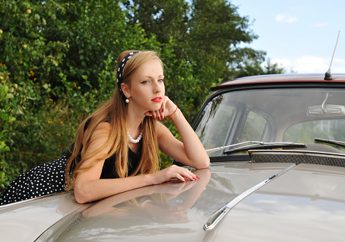 Portrait of pretty girl lean agains shining old car