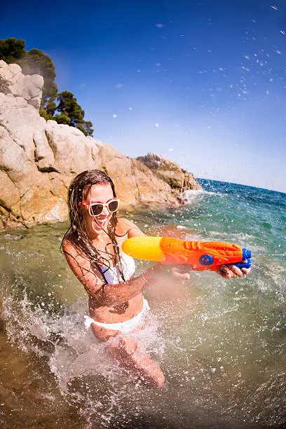 Girl enjoying water fight with water gun at the beach