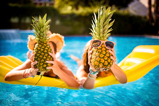 Girls having a silly time with pineapples in swimming pool