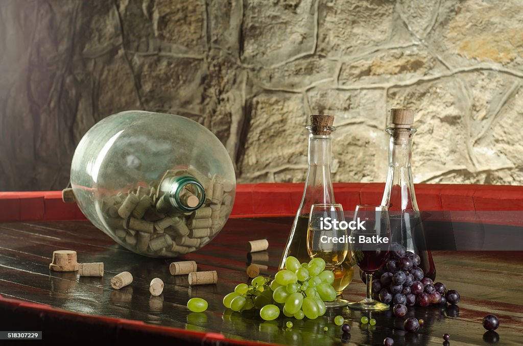 Still life with wine glasses, wine bottles and grapes A shot of still life with grapes, wine glasses, wine bottles and bottle with corks in old cellar. Aging Process Stock Photo