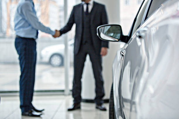 Buying new car at car showroom Handshake between two business people in a car showroom. car salesperson stock pictures, royalty-free photos & images