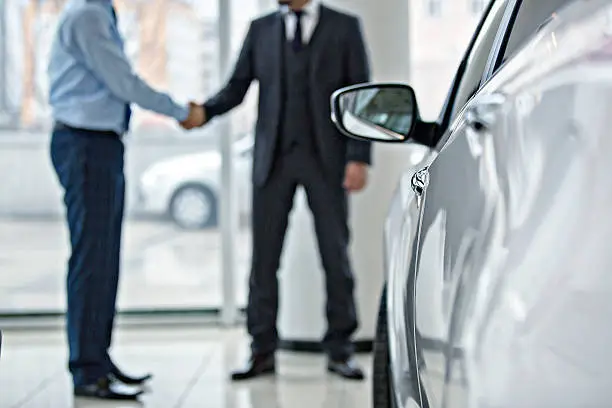 Handshake between two business people in a car showroom.