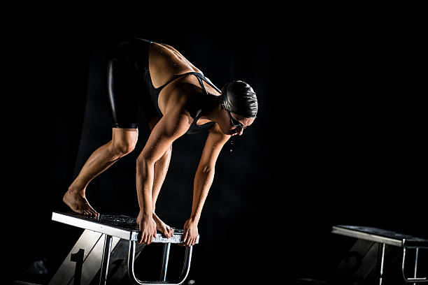 Swimmer On A Swimming Starting Block Professional female swimmer standing on the starting block and preparing to jump into an olympic pool.   starting block stock pictures, royalty-free photos & images