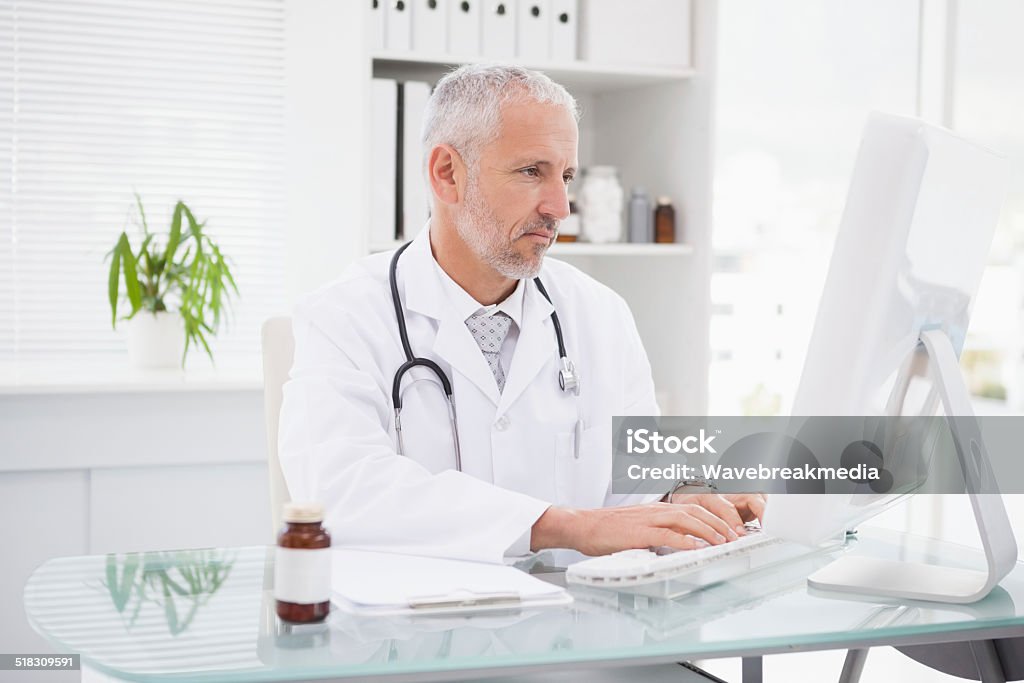 Happy doctor typing on keyboard Happy doctor typing on keyboard in medical office Doctor Stock Photo