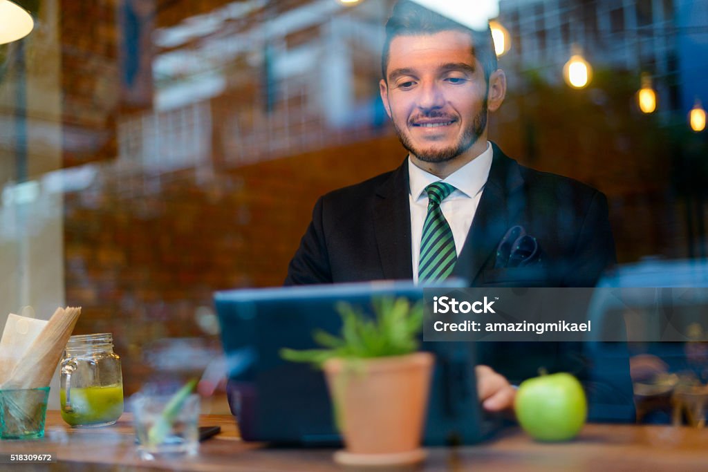 Businessman using laptop computer in coffee shop Businessman using laptop computer in coffee shop. Picture taken outside of coffee shop so reflections of the window can be seen. 30-34 Years Stock Photo