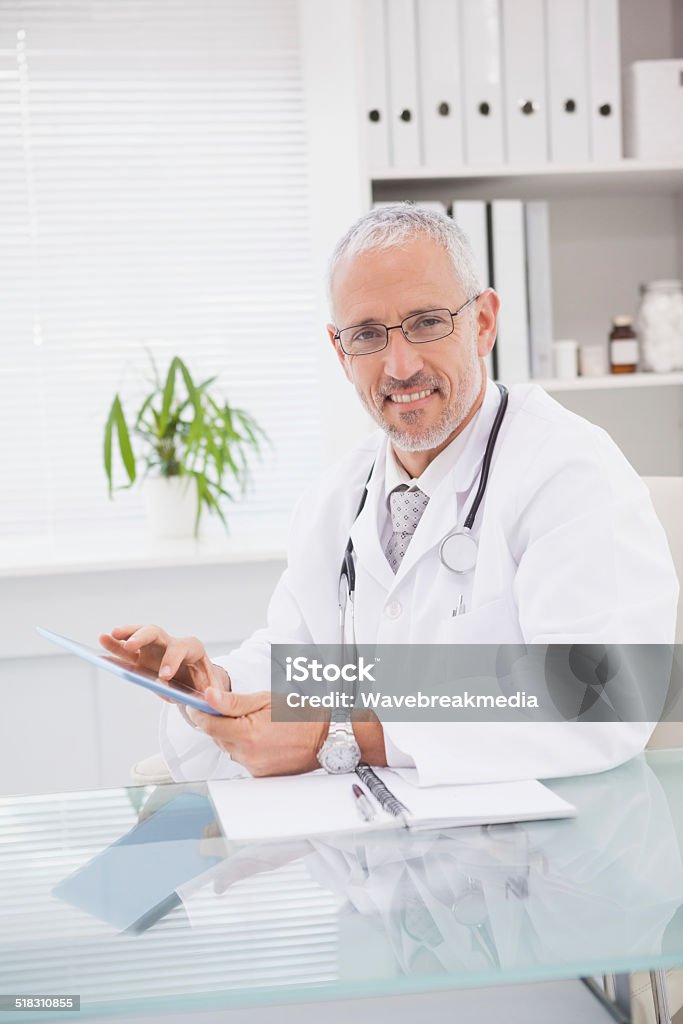 Smiling doctor using a tablet pc Smiling doctor using a tablet pc in medical office 40-49 Years Stock Photo