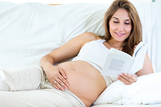 istock Pregnant woman reading a book on sofa. 518313773