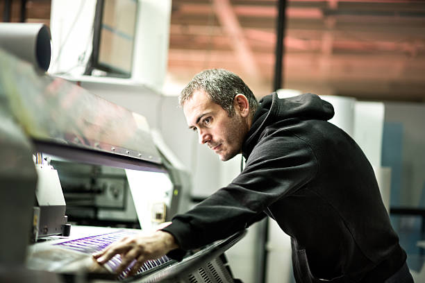 Male worker operating on industrial printer Skilled worker operating on industrial printer inside the printing factory. printing press stock pictures, royalty-free photos & images