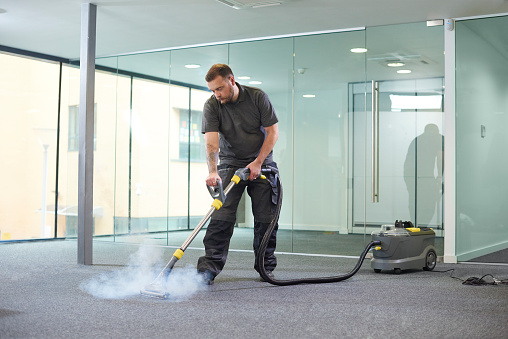 a male cleaning contractor steam cleans an office carpet in a empty office in between tenants.
