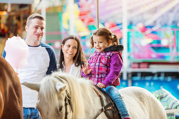 Girl enjoying pony ride, fun fair, parents watching her Little girl enjoying a ride on pony at fun fair, parents watching her, amusement park pony photos stock pictures, royalty-free photos & images