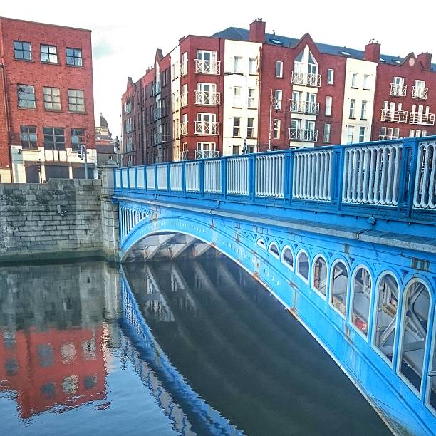 This image captures Dublin at sunset, highlighting the River Liffey running through the city center with multiple bridges crossing over it. On the right side, the Four Courts building with its iconic dome stands out as a landmark of Dublin’s historic architecture. The golden evening light reflects on the water and enhances the urban skyline, which combines cultural heritage with modern development. The perspective emphasizes Dublin’s role as a vibrant European capital, blending tradition, history, and contemporary life, making it a significant travel and tourism destination.