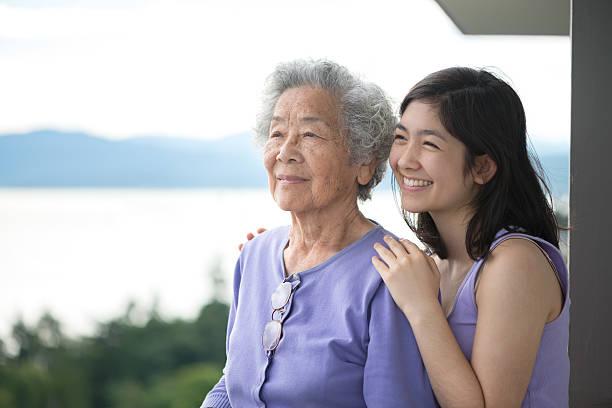 Senior Asian Woman and Granddaughter Enjoying View from Balcony Asian Grandmother and Eurasian granddaughter with park, water and mountains in background. 80 89 years photos stock pictures, royalty-free photos & images