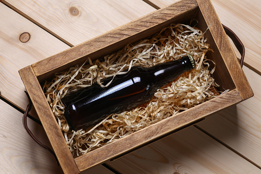 Bottle of beer in a wooden crate with wood shavings on a bright wooden surface