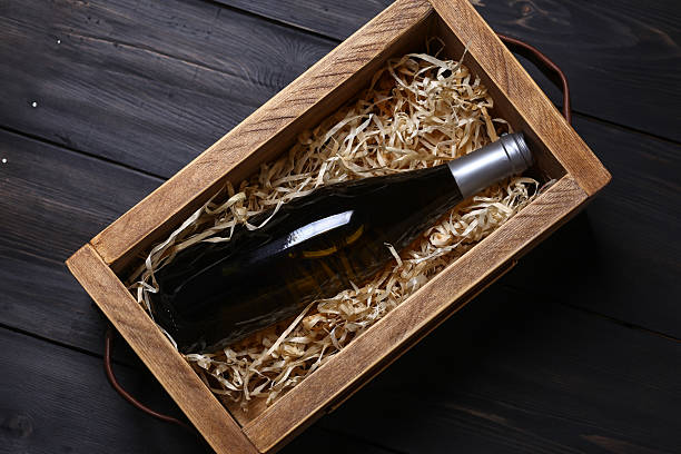 Wine bottle in a crate Bottle of white wine in a wooden crate with wood shavings on a dark wooden surface wine shipping stock pictures, royalty-free photos & images