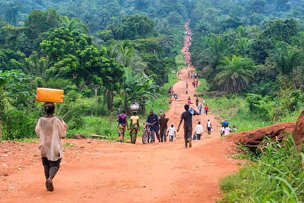 Rural Road with a lot of pedestrians, DR Congo Karawa, Democratic Republic of Congo - August 24, 2013: An upaved road in rural Congo, a lot of people are walking on the road which connects two villages in the province of Equateur. Walking and bicycling is nearly the only way of transportation in the poor regions of Congo. Mostly women are carrying heavy loads of goods on their heads when they are walking to a market place. central africa stock pictures, royalty-free photos & images
