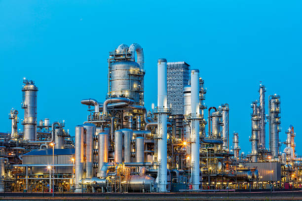 petrochemische fabrik beleuchtet bei dämmerung - destillationsturm stock-fotos und bilder