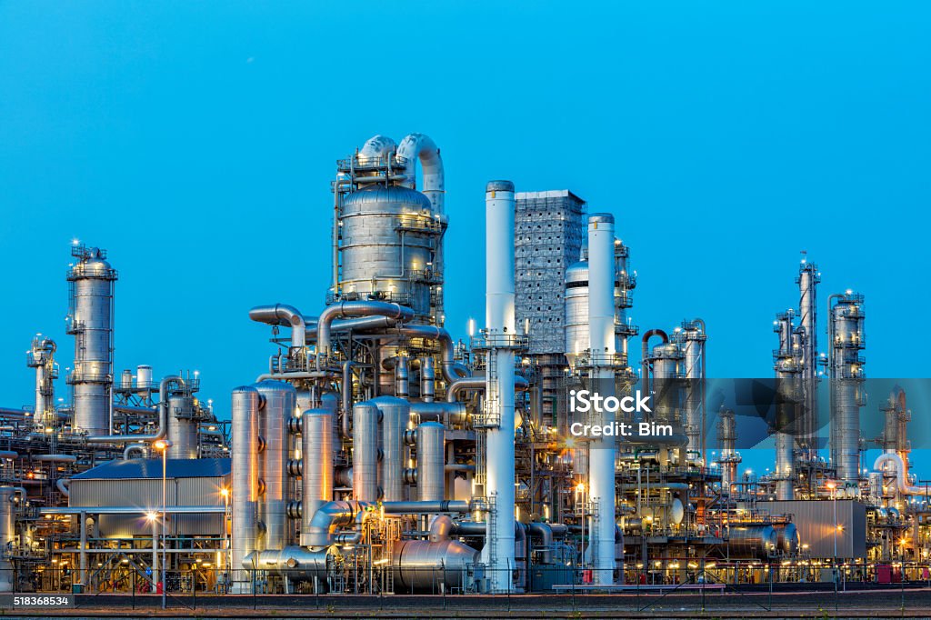 Petrochemical Plant Illuminated at Dusk A large, modern petrochemical plant at dusk in industrial district near Rotterdam, Netherlands, Benelux, Europe. Distillation towers and other installations are visible against blue sky. 50 megapixel image taken with Canon EOS 5Ds, digital blending technique, long exposure with tripod. Chemical Plant Stock Photo