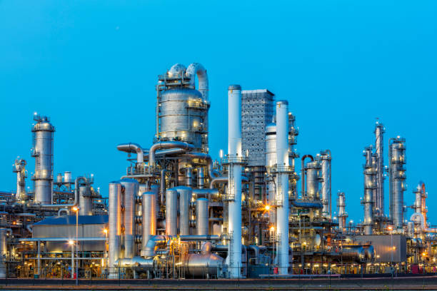 нефтехимический завод освещенной в сумерках - distillation tower стоковые фото и изображения