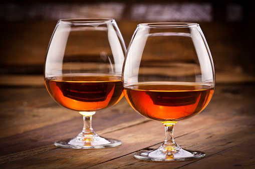 Front view of two cognac snifters shot on rustic wood table. Focus on the glass on foreground. Low key DSRL studio photo taken with Canon EOS 5D Mk II and Canon EF 70-200mm f/2.8L IS II USM Telephoto Zoom Lens