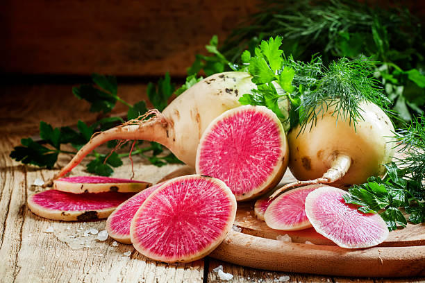 Slices of pink watermelon radish on a wooden table Slices of pink watermelon radish on a wooden table with parsley and dill, selective focus dikon radish stock pictures, royalty-free photos & images