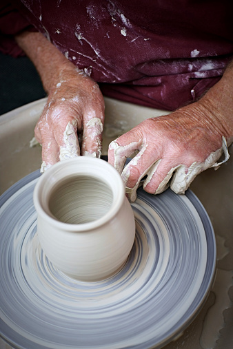 Top view of potter hands making a pot in traditional style on pottery wheel