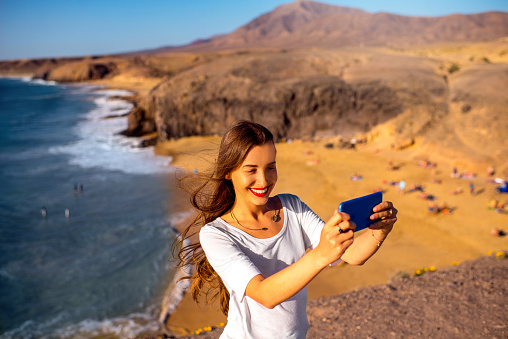 Young female tourist making selfie photo with Papagayo beach on the background on Lanzarote island in Spain