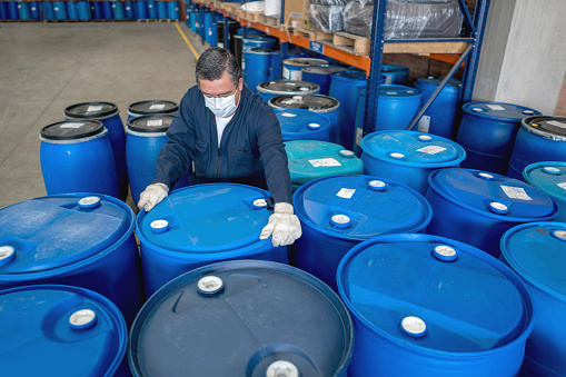 Man working at a chemical factory moving barrels with toxic products and wearing a facemask