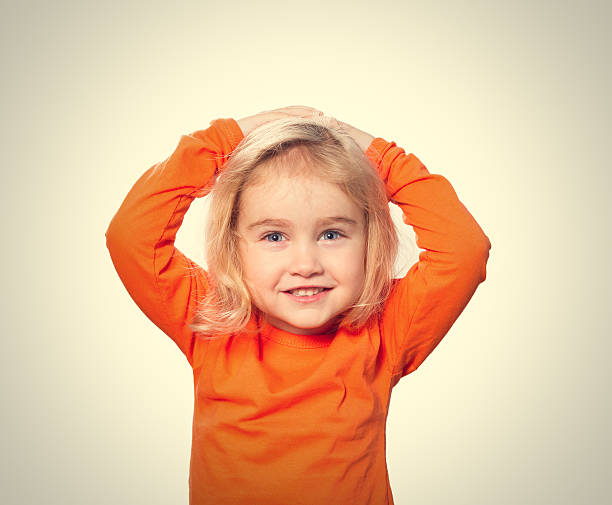 Little Funny girl in orange blouse holding his head. Isolated on gray  background