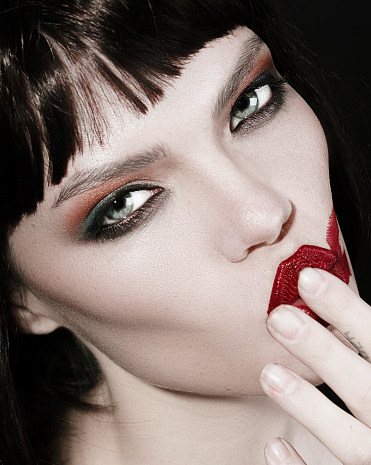 Portrait of a green eyed brunette with beautiful high-fashion make-up and red lips on a black background.