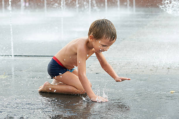 istock Happy kid playing in a fountain 518400557