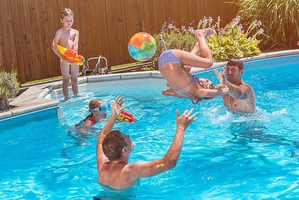 Young black man smiling while standing in water at swimming pool holding beach ball in hands on summer sunny day