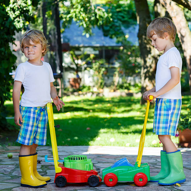 dois pouco, rapazes jogando com brinquedos de cortador de relva - gardening vegetable garden action planting imagens e fotografias de stock