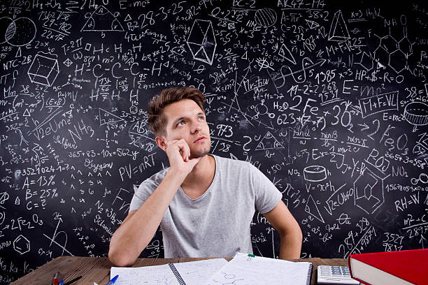 Thoughtful hipster student doing his homework in front of a big blackboard