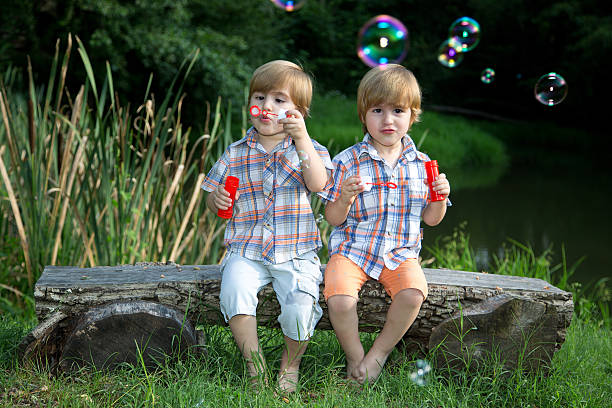 istock Twin Brothers Blowing Soap Bubbles in Summer Park 518424159