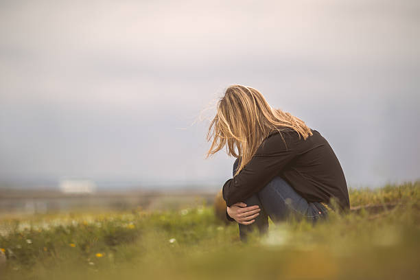 Depression in nature! Side view of a despaired woman sitting curled up in nature. hugging knees stock pictures, royalty-free photos & images