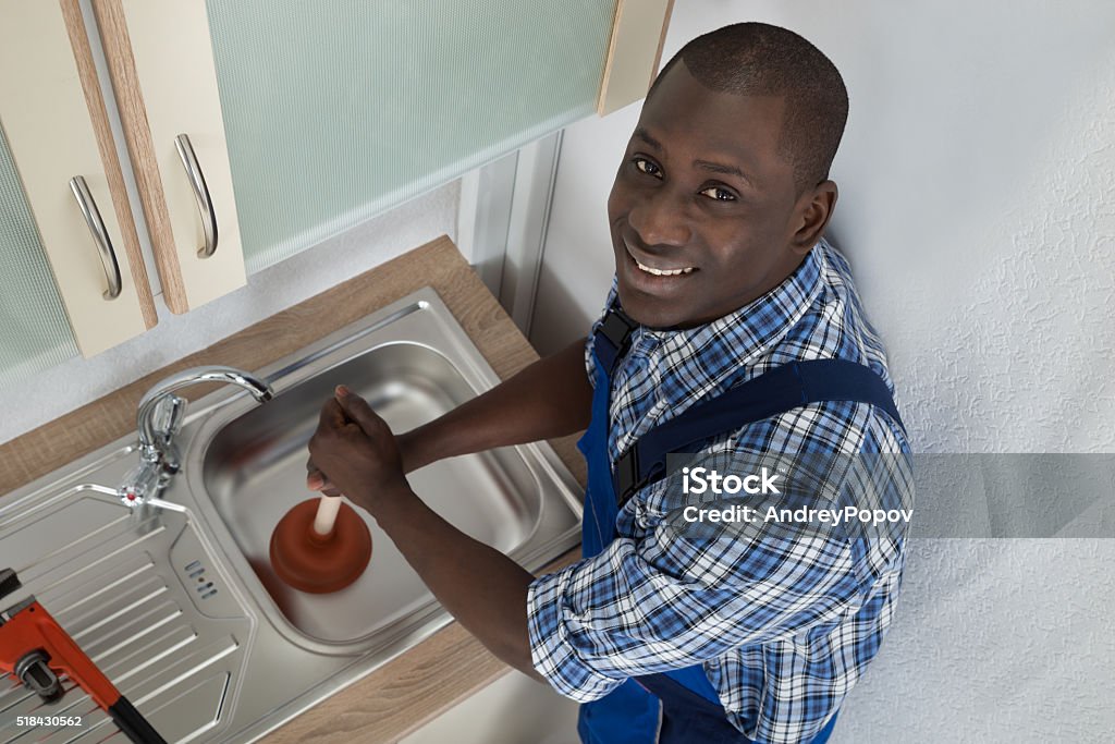 Plumber Using Plunger In Kitchen Sink Young Happy African Plumber Using Plunger To Unclog Kitchen Sink African Ethnicity Stock Photo