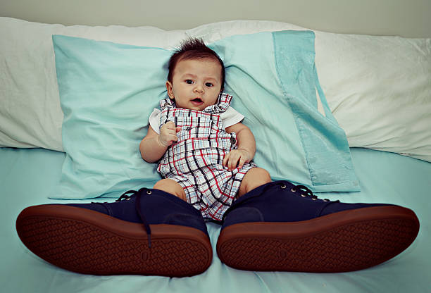 Asian Baby Wearing Big Shoes on The Bed Asian Baby Wearing Big Shoes on The Bed eccentric photos stock pictures, royalty-free photos & images