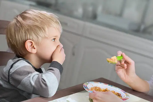 Photo of Blond boy holds hand on his mouth to stop eating