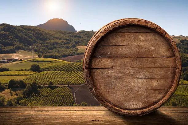 Photo of corkscrew and wooden barrel, vineyard on background
