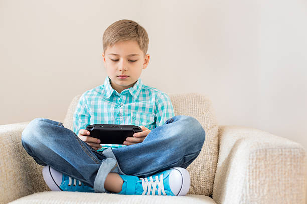 istock Boy playing hand-held video game on sofa at home 518456433