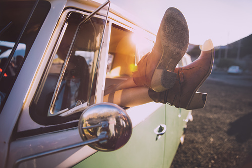 Young woman relaxing by crossing legs out of the window of a nice vintage van on sunset