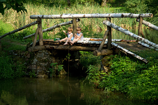 Adorable Little Twin Brothers Sitting on the Edge of Wooden Bridge and Fishing on Beautiful Lake at Summer