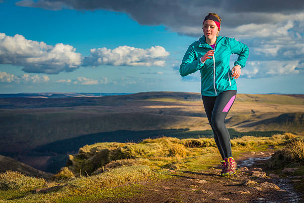 Young woman trail running along wilderness path on mountain top